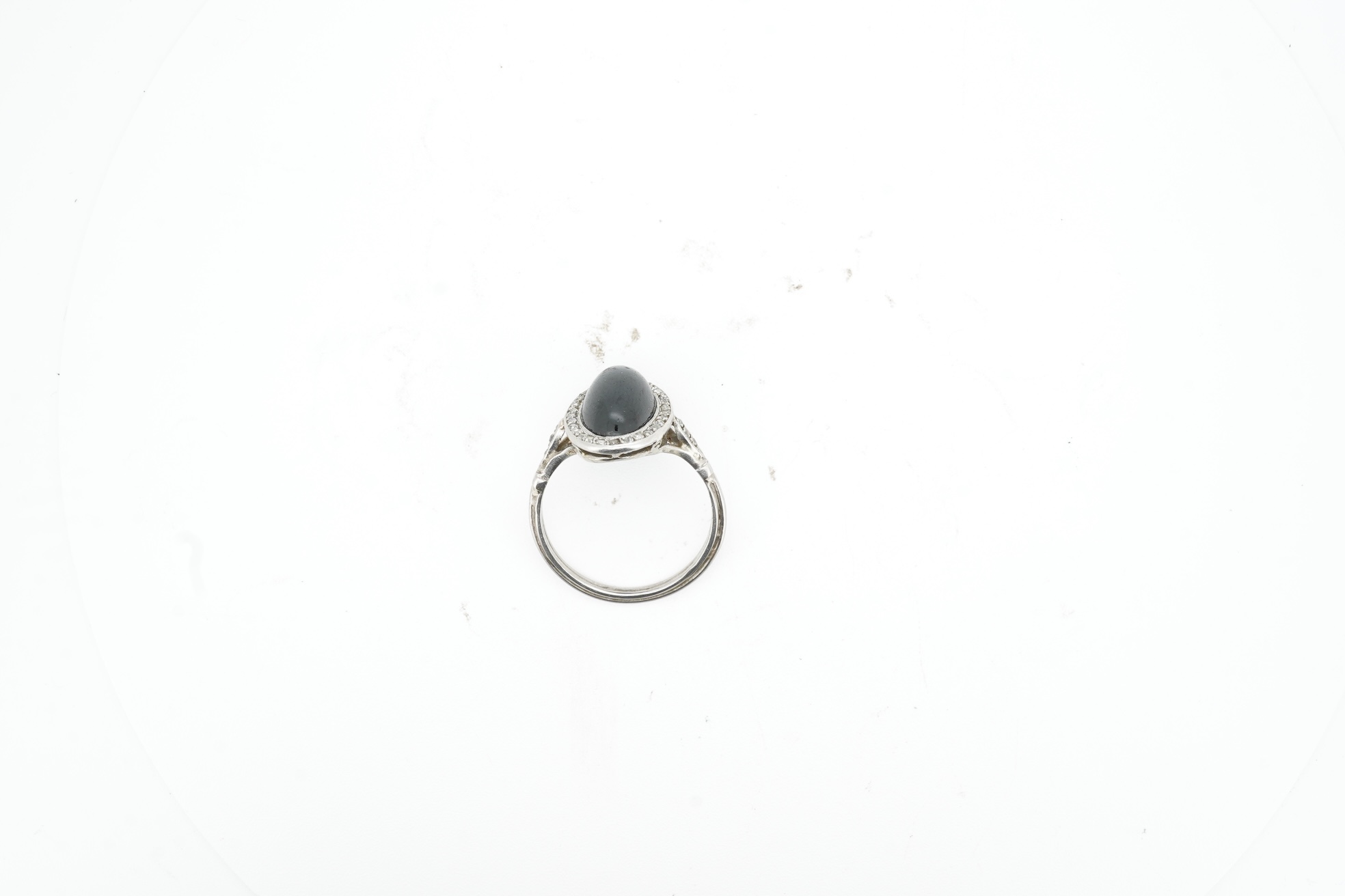 A sapphire and diamond ring, 1920s, set with a cabochon sapphire measuring approximately 2.4 x 6.8 x 4.7mm, within a border of rose-cut diamonds, mounted in platinum, size L1/2